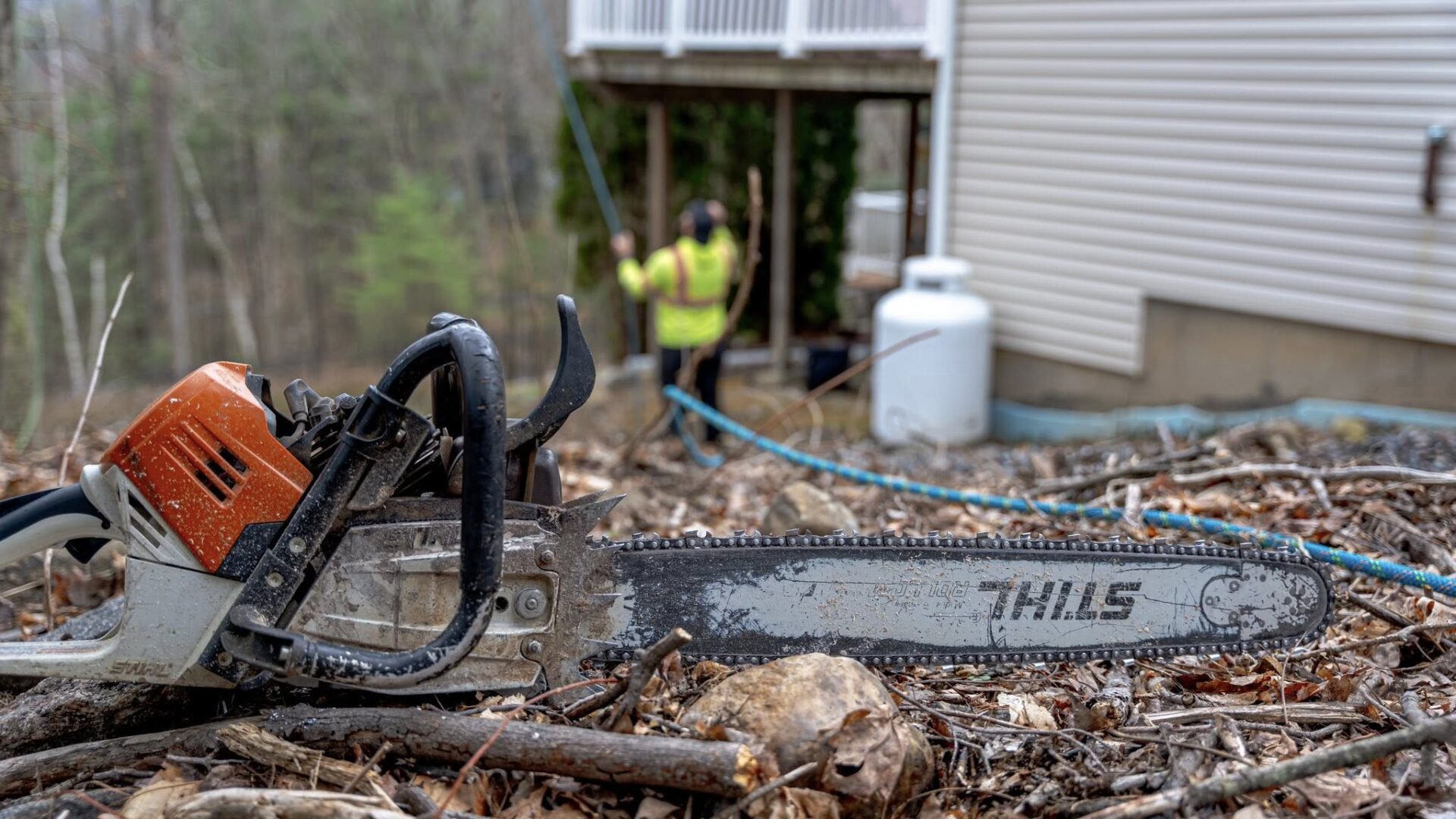 USA Tree Header Chainsaw in foreground with USA Tree Experts crew performing tree removal near a residential home in Connecticut